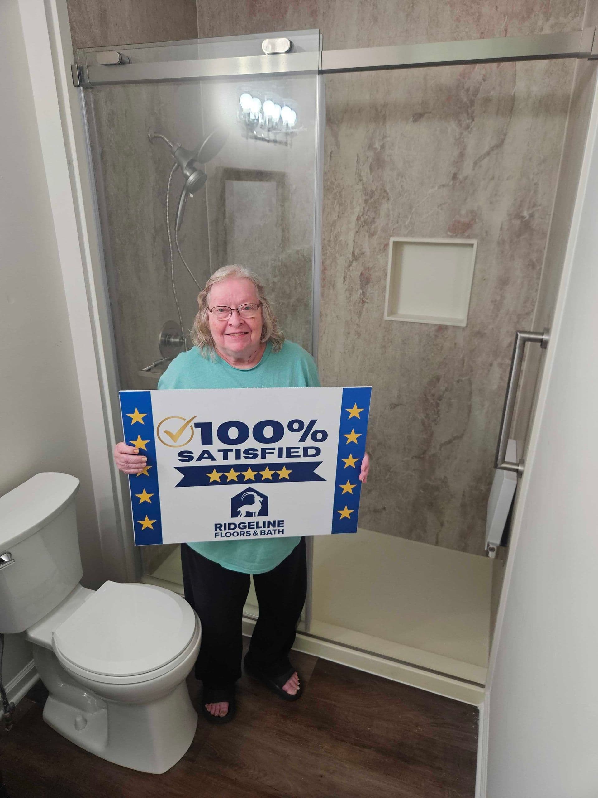 Satisfied customer holds 100% satisfied five-star review sign in newly remodeled bathroom with tiled shower enclosure and updated fixtures