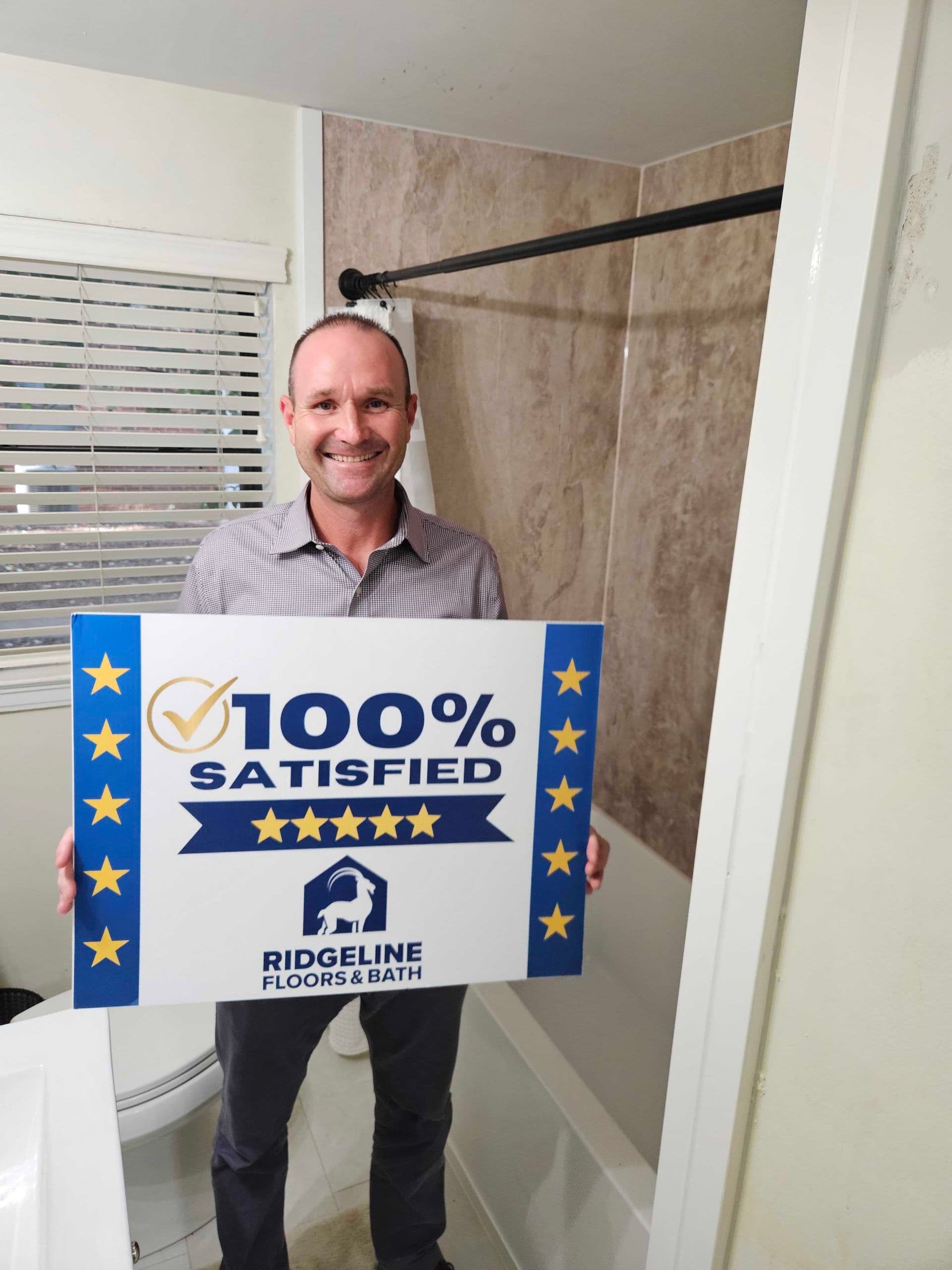 Man holding a 100% satisfied five-star customer review sign for Ridgeline Floors & Bath in a bathroom showroom